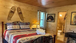 A wooden cabin bedroom with a bed, pillows, a nightstand, a lamp, and a wooden ceiling. - Bucksnort Lodge- Blue Ridge GA (Blue Ridge)