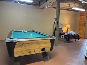 Ein Billardtisch mit einer Kugel, ein Bett mit Decke und eine Lampe in einem Raum mit Holzwänden und Deckenventilator.