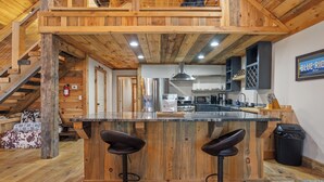 Un interior de madera con una zona de cocina, una barra con taburetes y una escalera.