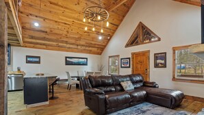 Un espacio habitable amplio con sofá de cuero, piso de madera, una mesa de comedor con sillas y una zona de cocina con refrigerador.