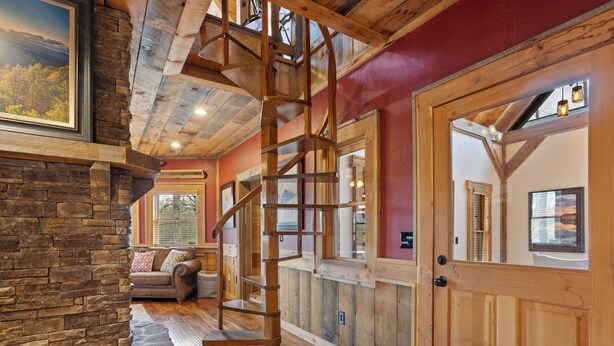 Une pièce spacieuse avec un escalier en bois, des murs en pierre et une grande porte.