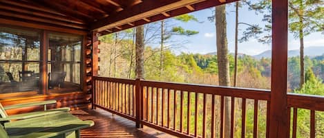 A wooden deck with picnic tables and a view of a forested landscape.