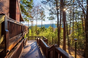 Une terrasse en bois menant à un chalet offrant une vue sur une forêt et des montagnes.