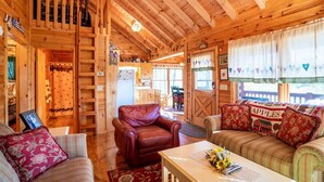 A cozy cabin interior with a wooden interior, a leather chair, a sofa with floral cushions, and a dining area. - Hog Heaven - Cherry Log GA (Cherry Log)