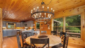 L’intérieur d’un chalet en bois comprend une table à manger ronde, des chaises, un lustre et un coin cuisine avec des placards et un four à micro-ondes.