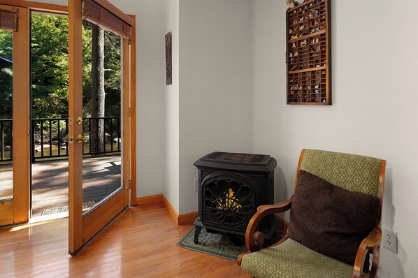 A room with a wooden floor, a green and brown chair, a black wood-burning stove, and a wall-mounted shelf with various items. - Rivers D Lite - Blue Ridge GA (Blue Ridge)