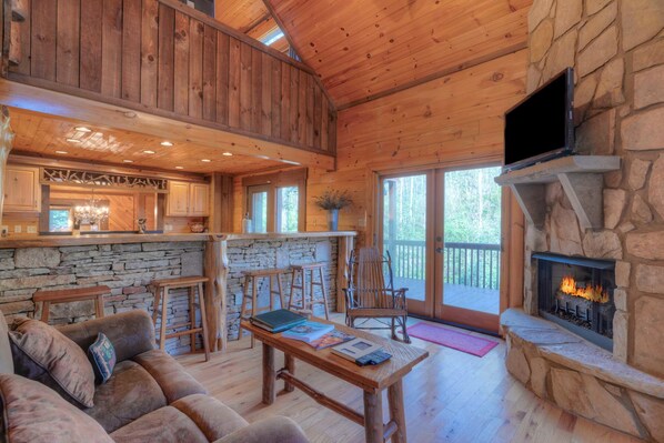 A rustic cabin interior with a stone fireplace, wooden furniture, and a stone wall. - Rushing Waters- Blue Ridge GA (Blue Ridge)