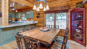 A wooden cabin interior with a large dining table, rustic chairs, a kitchen area, and a decorative cabinet. - Sky Ridge - Blue Ridge GA (Blue Ridge)