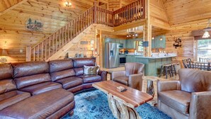 A wooden cabin interior with a leather sofa, a dining table, and a kitchen area. - Sky Ridge - Blue Ridge GA (Blue Ridge)