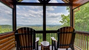 A wooden deck with two Adirondack chairs and a small table, overlooking a forested landscape. - Sky Ridge - Blue Ridge GA (Blue Ridge)