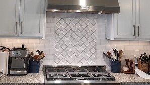 A modern kitchen with light blue cabinets, a stainless steel stove, and a large range hood.