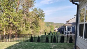 A residential backyard with a lawn, a black metal fence, and a house with a covered patio.