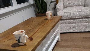 A wooden coffee table with two mugs, a white cabinet, and a patterned sofa in a room with wooden flooring.