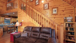 L’intérieur d’un chalet chaleureux, avec un canapé en cuir, un escalier en bois et une bibliothèque.