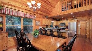 L’intérieur d’un chalet en bois comprend un coin repas, une cuisine et de grandes fenêtres donnant sur une forêt.