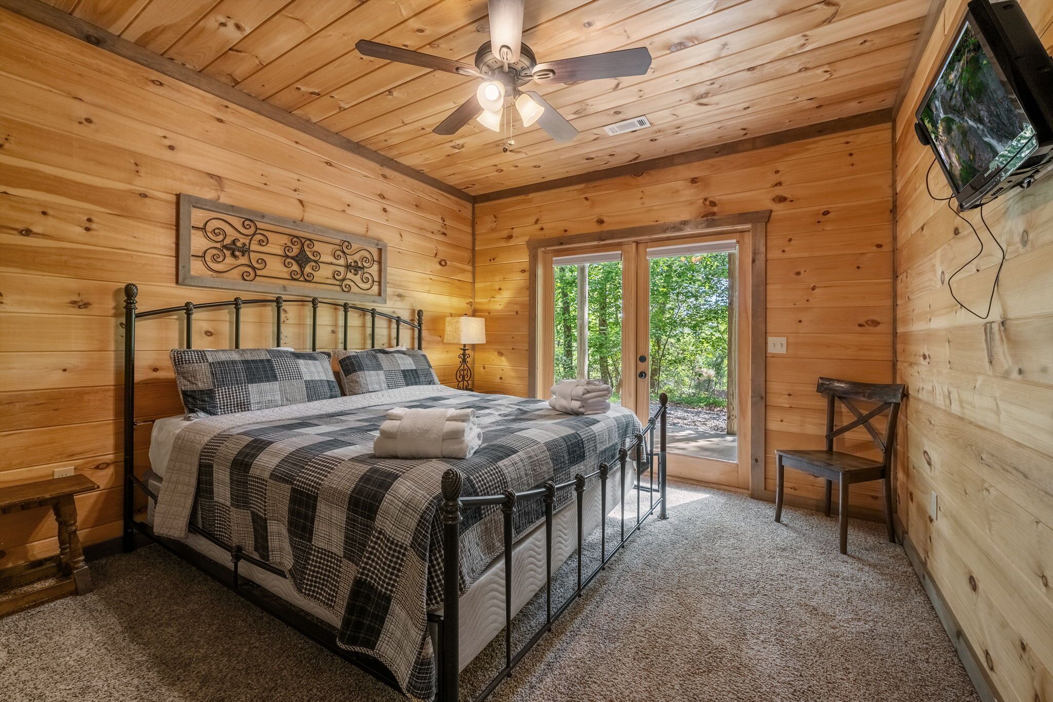 Une chambre dans un chalet en bois, avec un lit, un ventilateur de plafond, une télévision et une fenêtre.