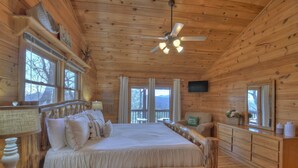 A wooden cabin bedroom with a bed, a dresser, a television, and a ceiling fan. - A Walk In The Clouds- Cherry Log GA (Cherry Log)
