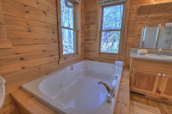 Une salle de bain rustique, avec une grande baignoire, des meubles en bois et une fenêtre donnant sur la forêt.