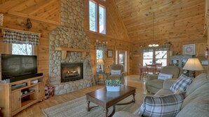A cozy cabin interior with a stone fireplace, wooden walls, a television, and a comfortable seating area. - A Walk In The Clouds- Cherry Log GA (Cherry Log)