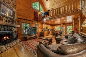 A cozy cabin interior with a stone fireplace, leather sofa, and a balcony with a dog. - A Creek Runs Thru It - Cherry Log (Cherry Log)