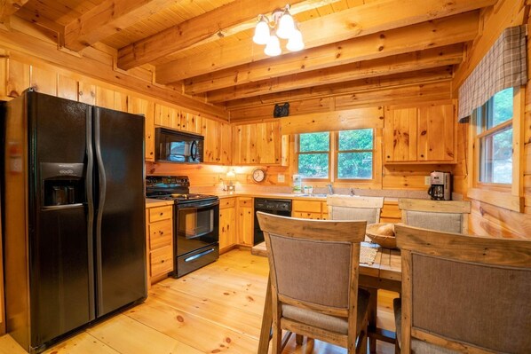 Interior de una cabaña de madera con cocina equipada, que incluye refrigerador, estufa, microondas y comedor con sillas.