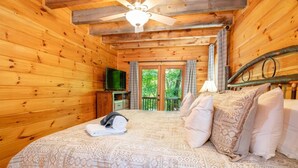 Een houten kamer met een bed, een televisie en een balkon met gordijnen.