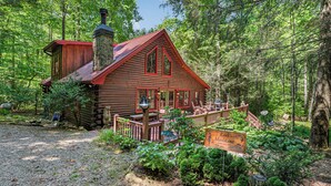 Une cabane rustique en rondins de bois, avec un toit rouge, entourée d’une forêt dense.