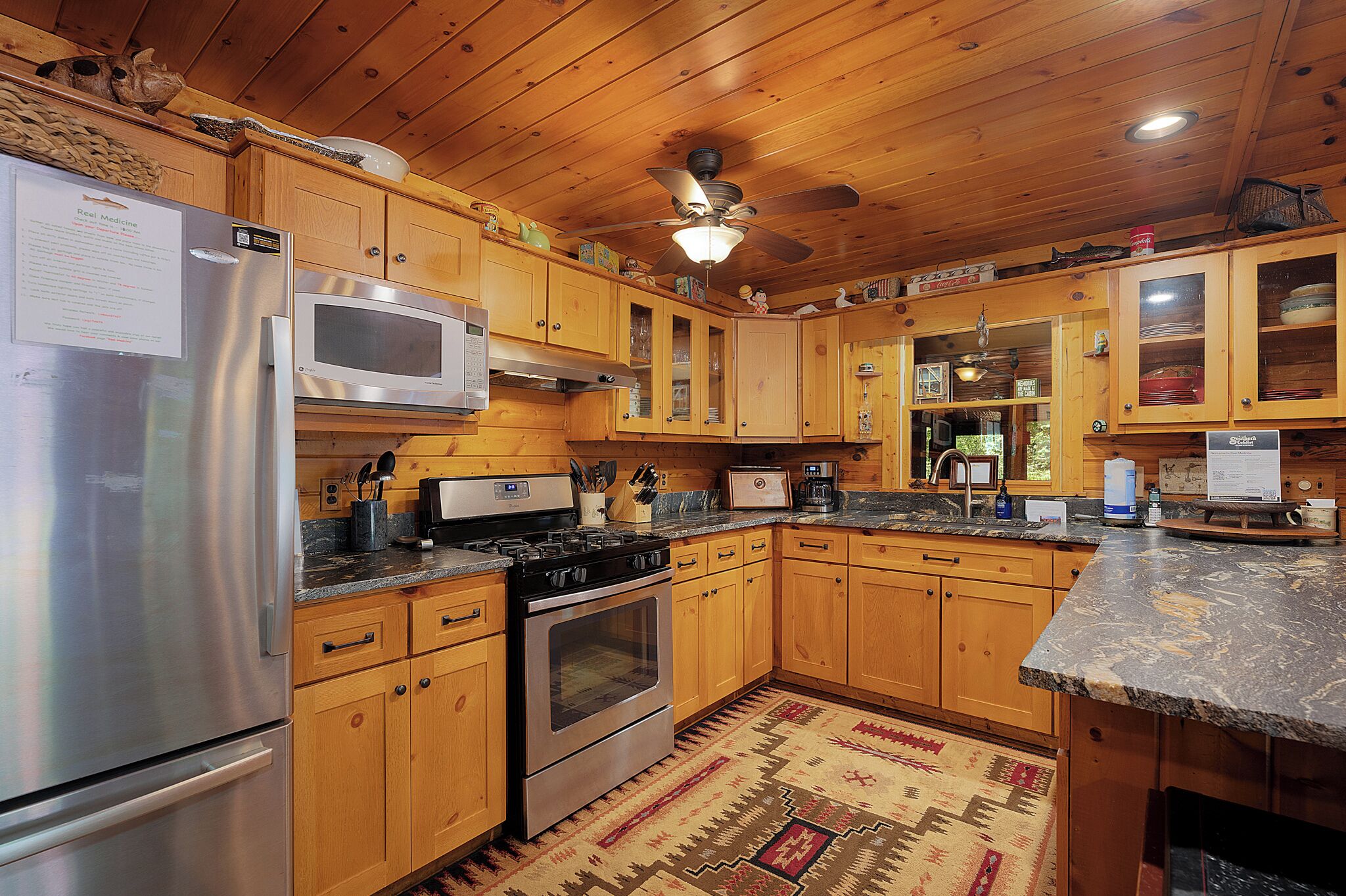 A kitchen with wooden cabinets, stainless steel appliances, and a patterned rug.