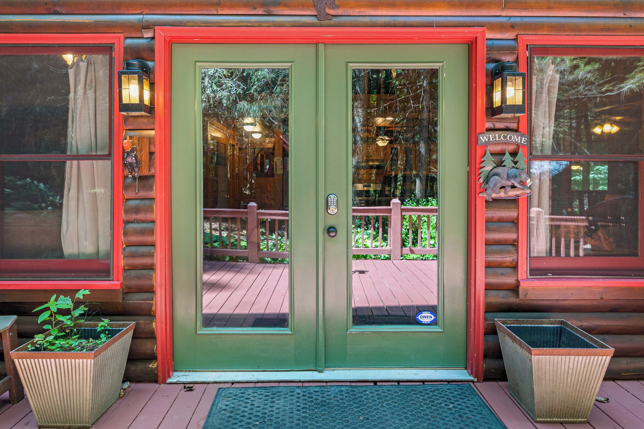 A log cabin with a green door, a welcome sign, and a wooden deck.