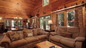 Un intérieur chaleureux de chalet en bois, avec deux canapés, un coin repas et de grandes fenêtres.