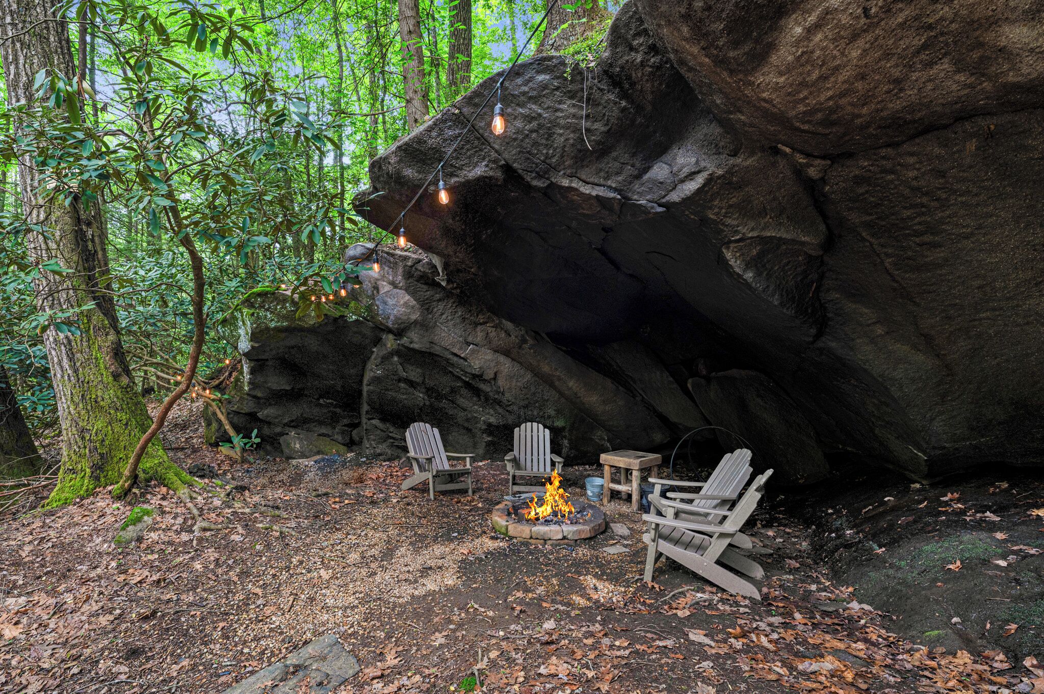 A rustic outdoor seating area with Adirondack chairs and a fire pit surrounded by a natural forest setting.
