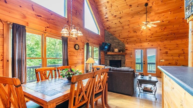 A wooden cabin interior with a dining area, sofa, fireplace, and kitchen counter. - Hawk's Hideaway- Blue Ridge GA (Mineral Bluff)