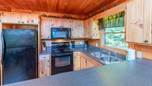 A compact kitchen with wooden cabinets, a black refrigerator, a microwave, an oven, and a sink. - Hawk's Hideaway- Blue Ridge GA (Mineral Bluff)