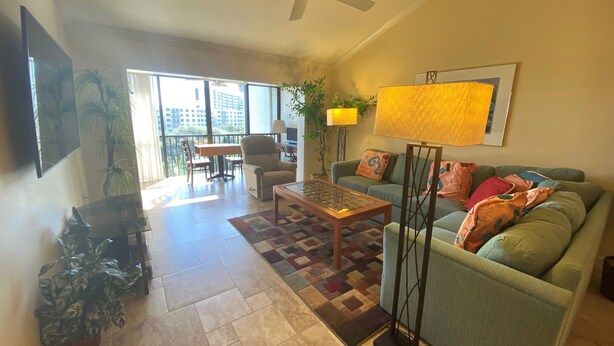 A living room with a sofa, coffee table, and a ceiling fan. There is a window with a view of buildings outside. - Charming Sunset views (Sarasota)