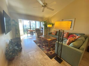 A living room with a sofa, coffee table, and a ceiling fan. There is a window with a view of buildings outside. - Charming Sunset views (Sarasota)