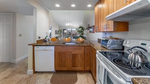 A modern kitchen with wooden cabinets, a built-in dishwasher, a stove with a kettle, and a toaster. - Charming Sunset views (Sarasota)