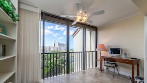 A room with a desk, chair, computer, and a view of a building through large windows. - Charming Sunset views (Sarasota)