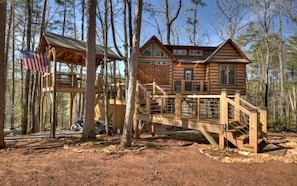 Une cabane en bois dotée d’une terrasse et d’un espace abrité, entourée d’arbres.