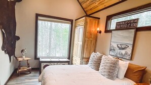A bedroom with a large bed, a window with a view of trees, a mounted animal head, and a sign with a quote. - Misty Mountain Treehouse- Blue Ridge GA (Morganton)