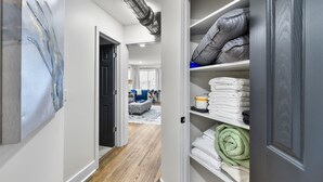 Un pasillo con piso de madera, un cuadro a la izquierda y un armario con toallas dobladas y almohadas a la derecha.