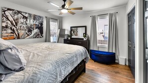 Un dormitorio con cama, ventilador de techo, cómoda, espejo y ventana con cortinas.