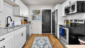 Una cocina moderna con armarios blancos, electrodomésticos de acero inoxidable, una puerta negra y una alfombra estampada.