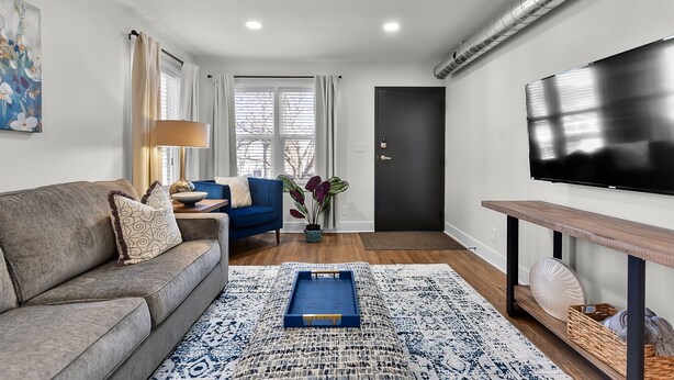 Una sala de estar moderna con un sofá, un sillón azul, una mesa de centro, un televisor y una alfombra estampada.