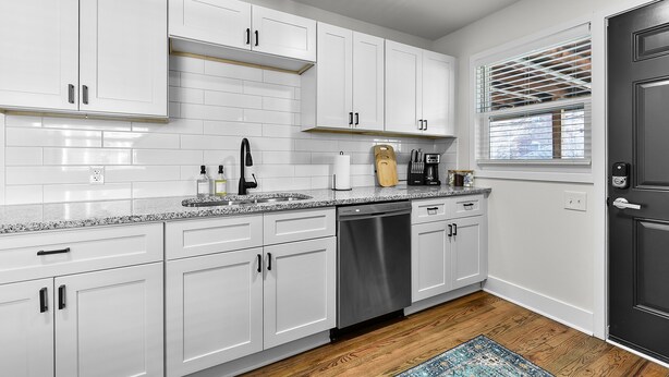 A modern kitchen with white cabinets, stainless steel appliances, and a wooden floor.