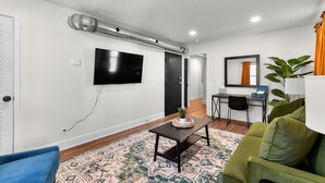 A modern living room with a flat-screen TV, a dining area with a small table and chairs, and a green sofa.
