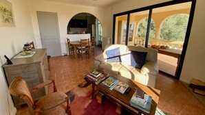 A spacious living area with a sofa, a coffee table, and a dining table. There is a kitchen in the background with an archway leading to another room. - Appartment in charming old country house (Vence)