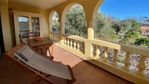 A balcony with a wooden chair and table, a view of trees and houses, and a tiled floor. - Appartment in charming old country house (Vence)