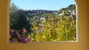 A view through an arched window of a town with buildings, greenery, and a clear sky. - Appartment in charming old country house (Vence)