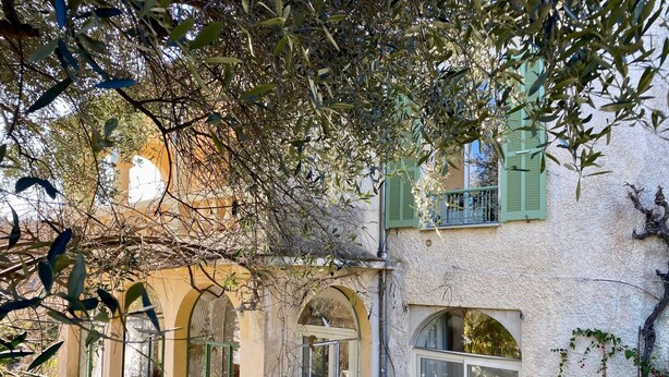 A rustic building with arched windows, a balcony with green shutters, and various potted plants around the exterior. - Appartment in charming old country house (Vence)