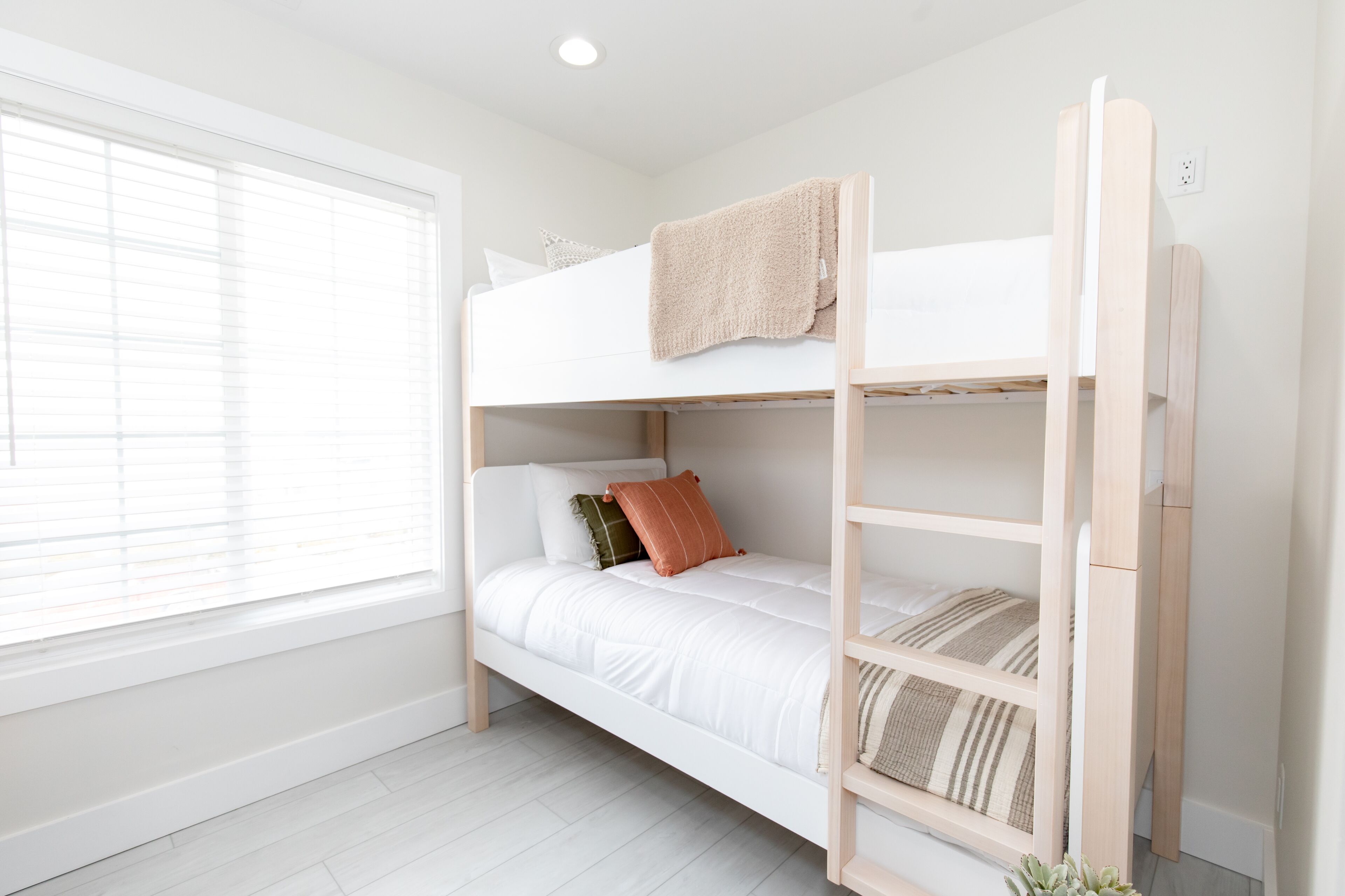 A bunk bed with a ladder, white bedding, and a window with blinds.